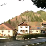 Maisons de Cervens éclairées par le soleil au pied d’une colline boisée