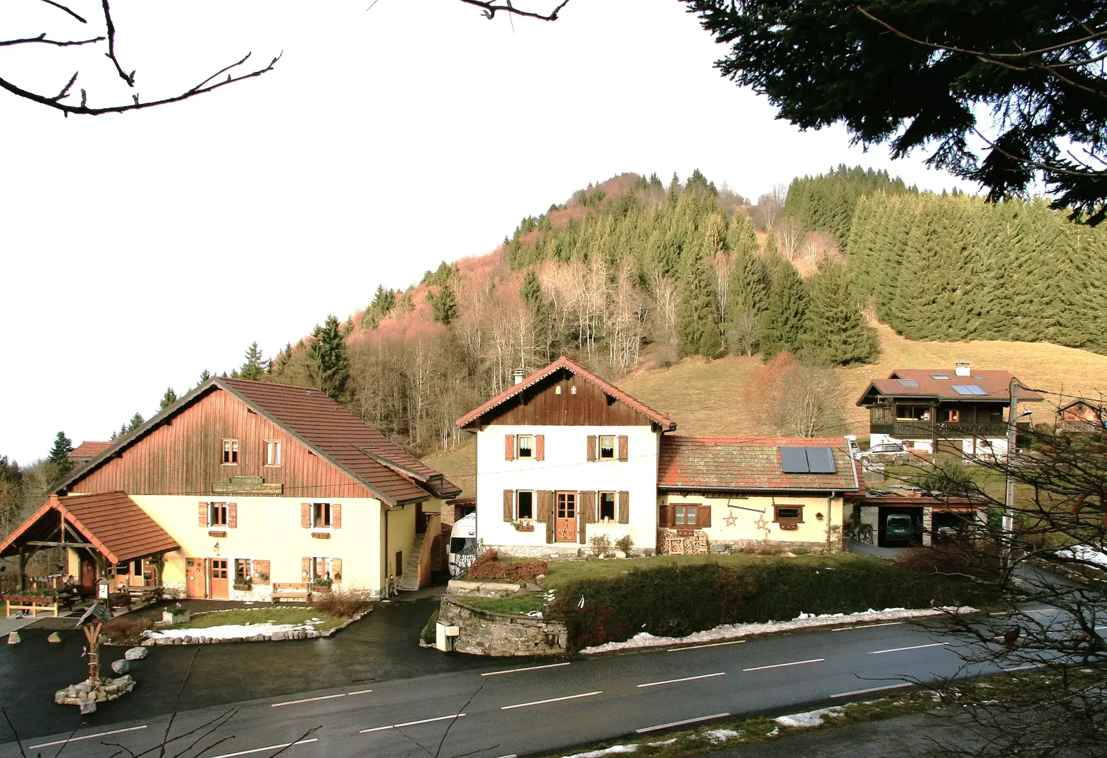 Maisons de Cervens éclairées par le soleil au pied d’une colline boisée