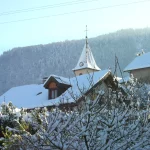 Clocher de l’église de Cervens derrière les toits et les arbres enneigés
