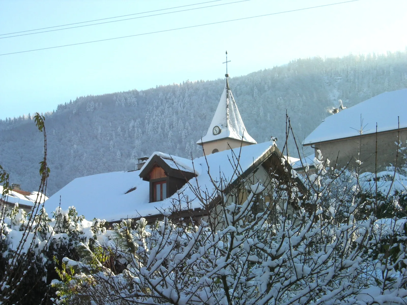 Clocher de l’église de Cervens derrière les toits et les arbres enneigés